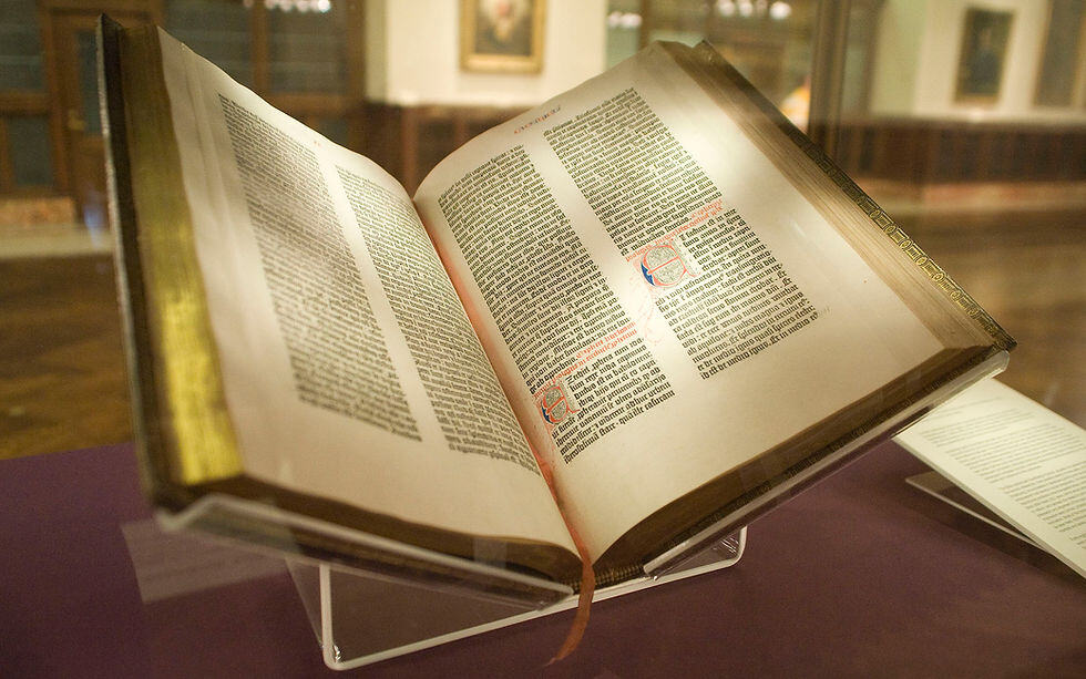 An open copy of the Gutenburg bible showing the printed text complemented by ornate embellishments.